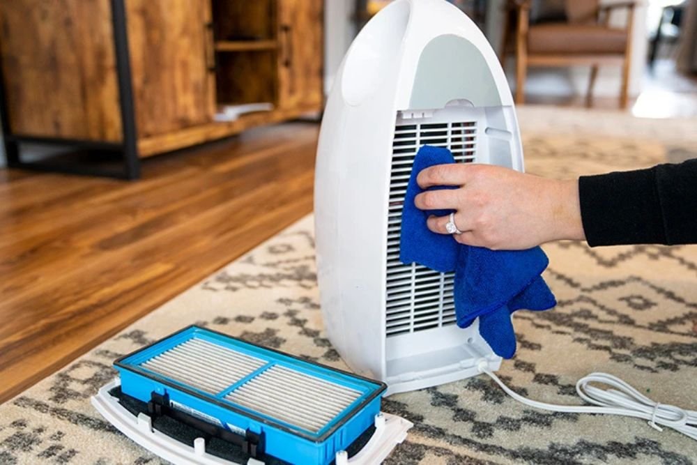 A person is seen cleaning a small air purifier with a blue cloth, related to appliance repair services in Fresno, CA.